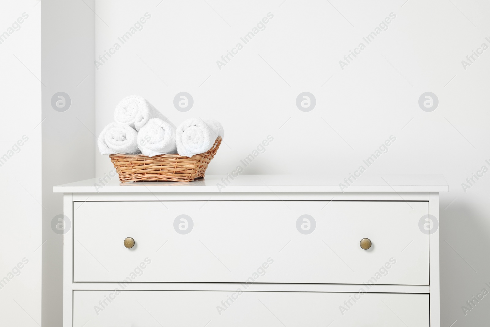 Photo of Soft rolled towels in wicker basket on white chest of drawers
