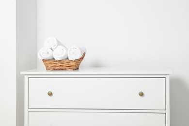 Photo of Soft rolled towels in wicker basket on white chest of drawers
