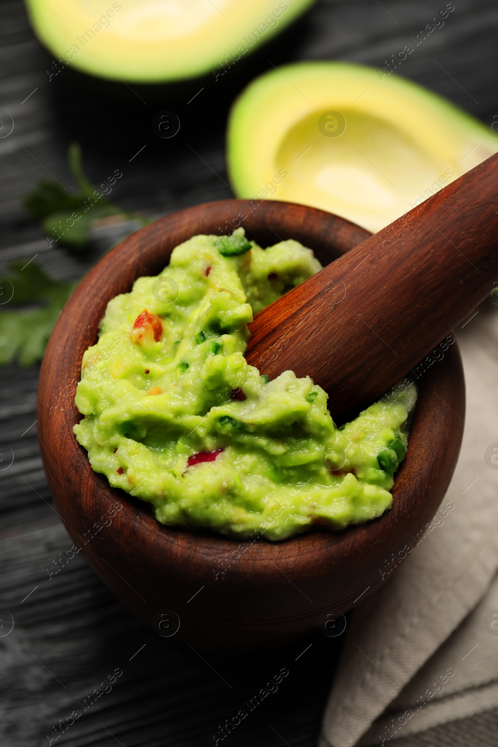 Photo of Mortar with delicious guacamole and ingredients on black wooden table, closeup