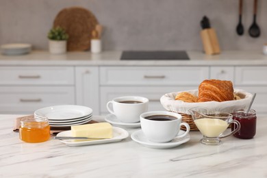 Photo of Breakfast served in kitchen. Fresh croissants, coffee, butter, jam, honey and sweetened condensed milk on white table