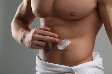 Man applying moisturizing cream onto his body on grey background, closeup