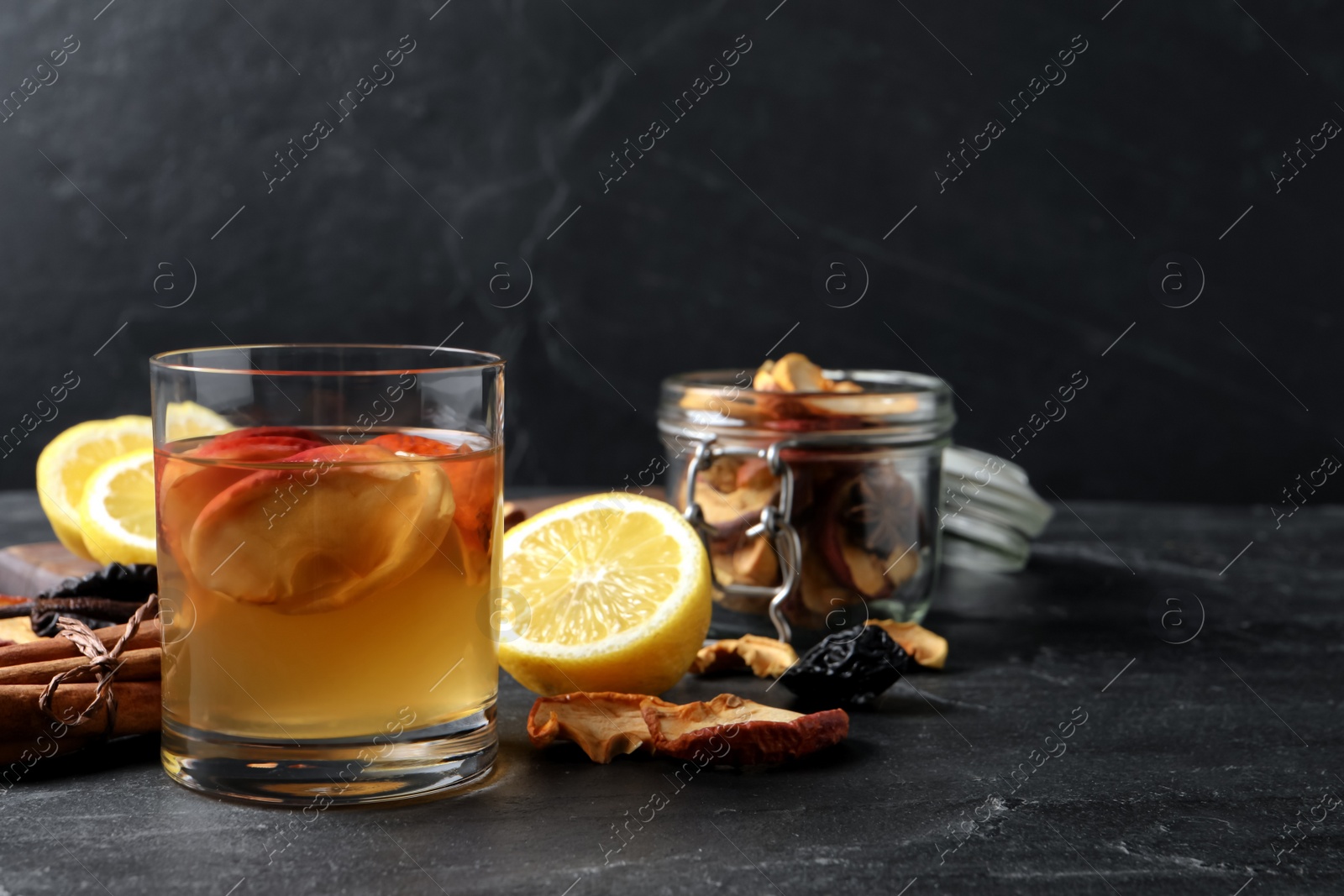 Photo of Delicious compote with dried apple slices and ingredients on black table, space for text
