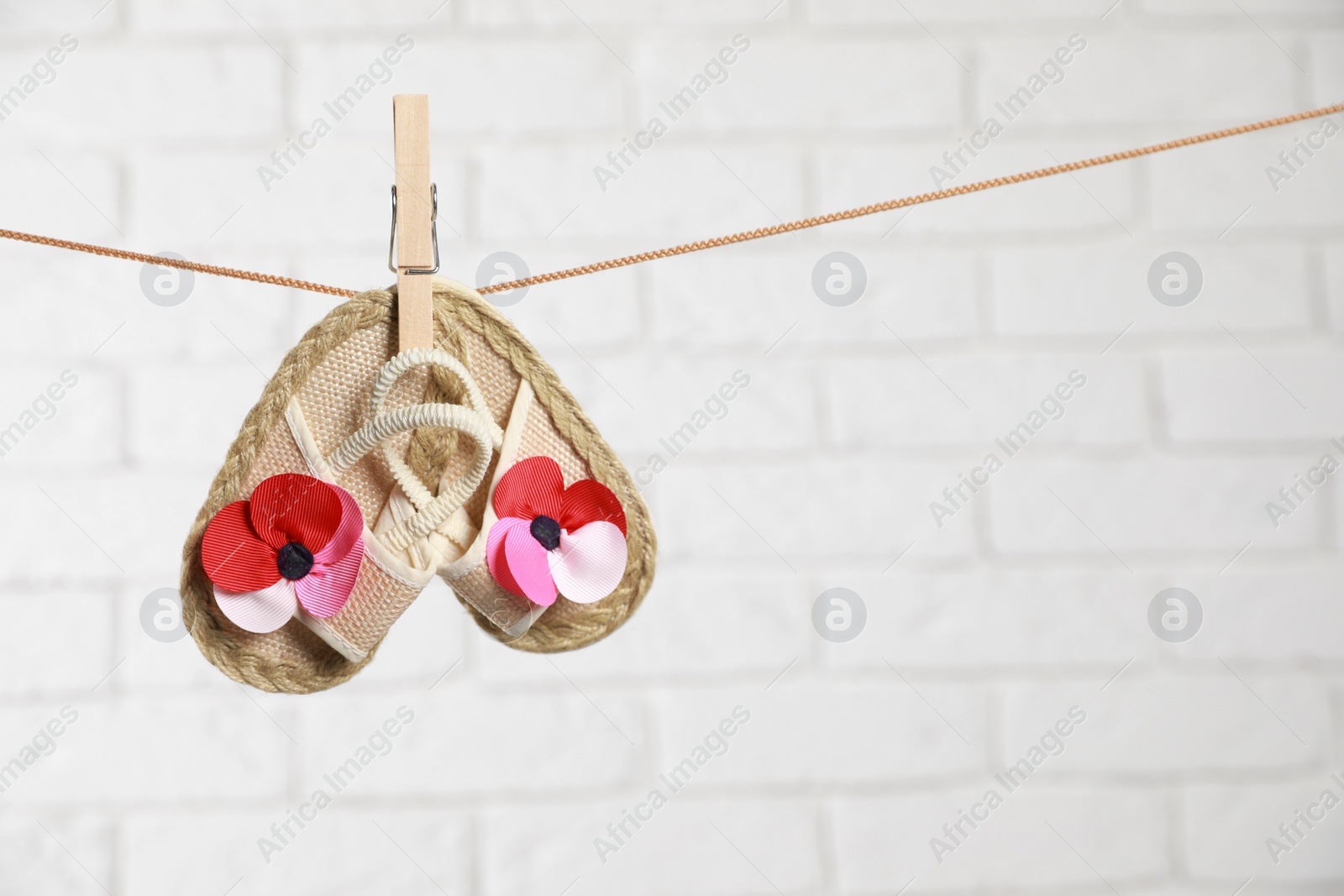 Photo of Cute baby shoes drying on washing line against white brick wall. Space for text