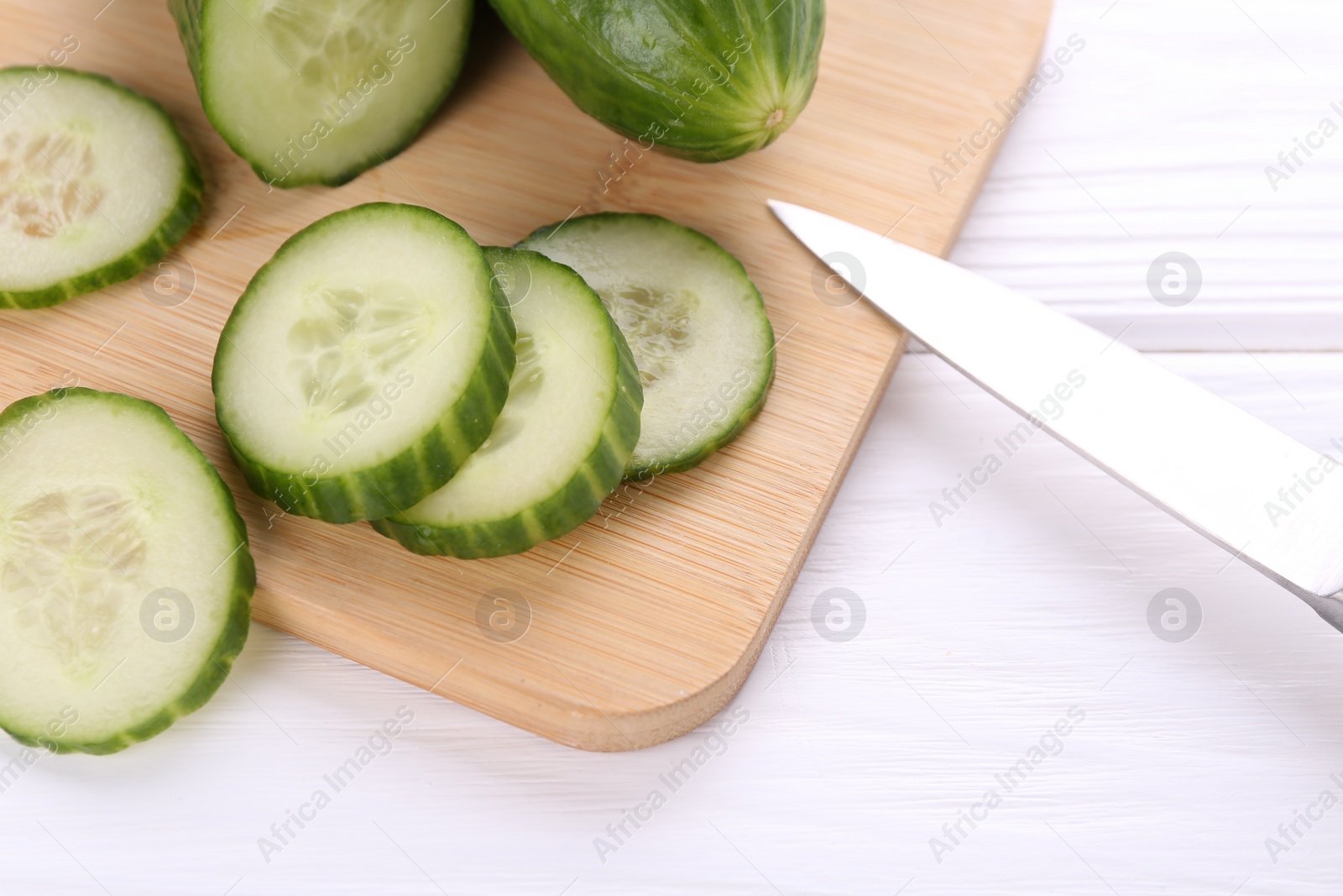 Photo of Cut cucumber, knife and wooden board on white table, above view
