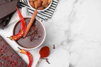 Cup of hot chocolate with chili pepper and cinnamon on white marble table, flat lay. Space for text