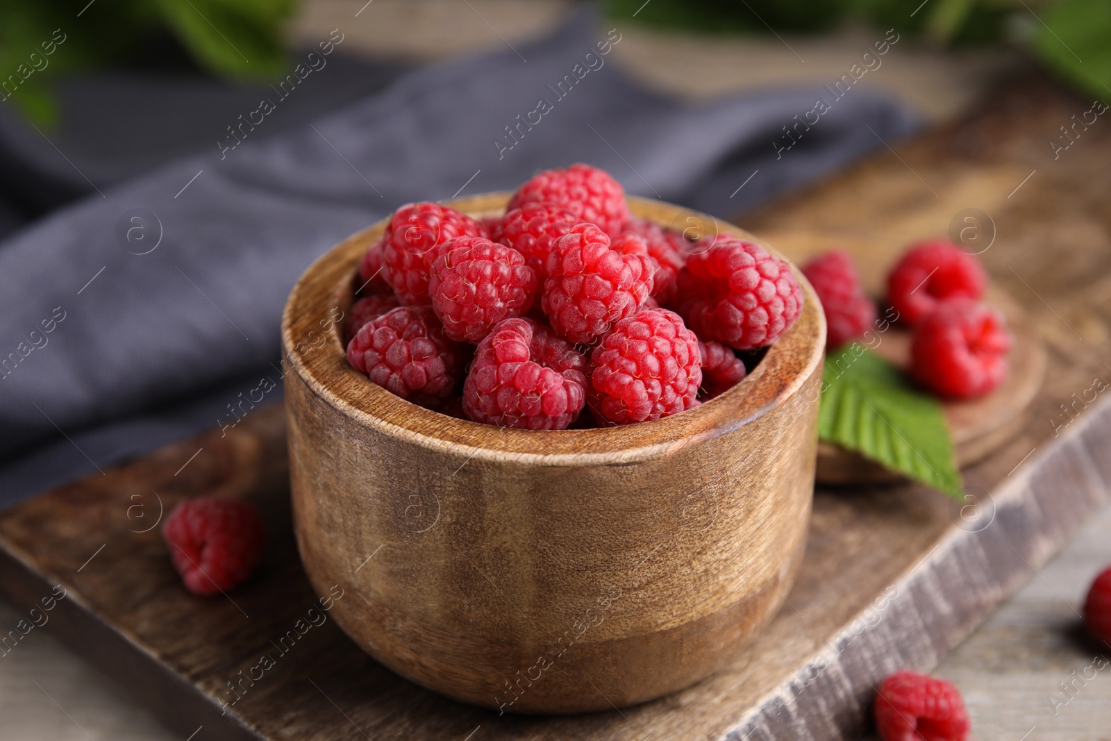 Photo of Bowl of fresh ripe raspberries on wooden board, closeup