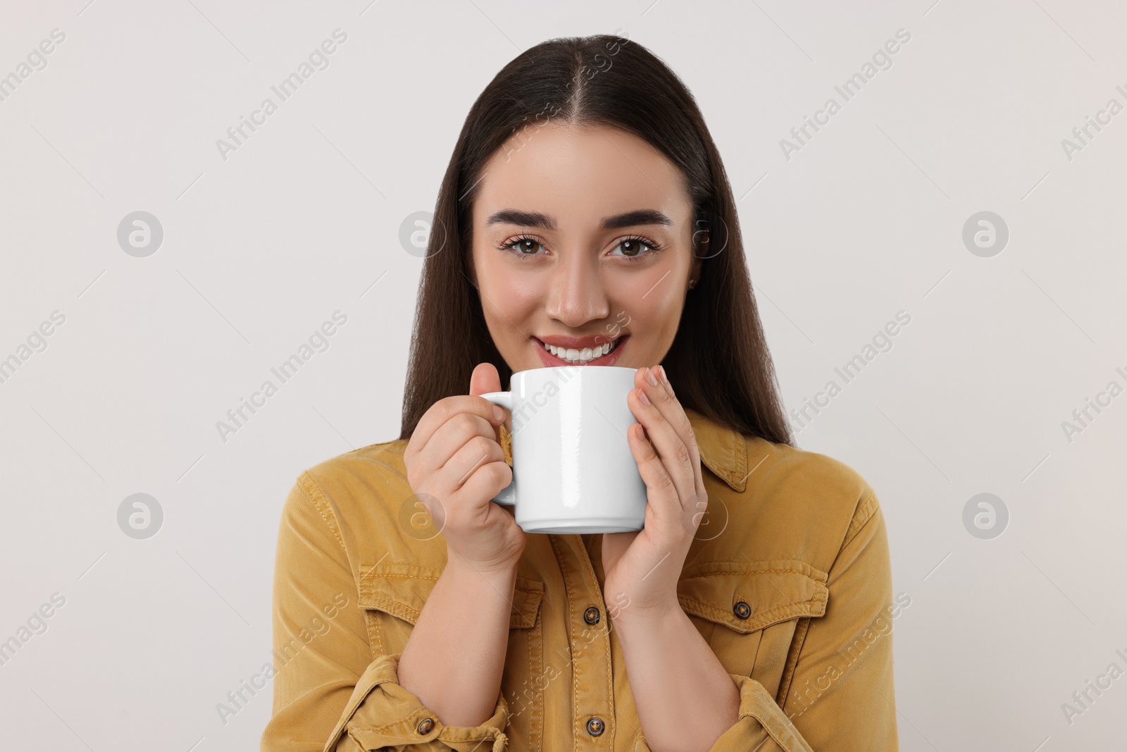 Photo of Happy young woman holding white ceramic mug on light grey background