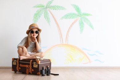 Photo of Adorable little child playing traveler with suitcase indoors