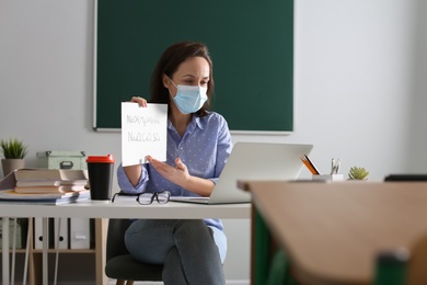 Teacher with protective mask conducting online lesson in classroom during COVID-19 quarantine