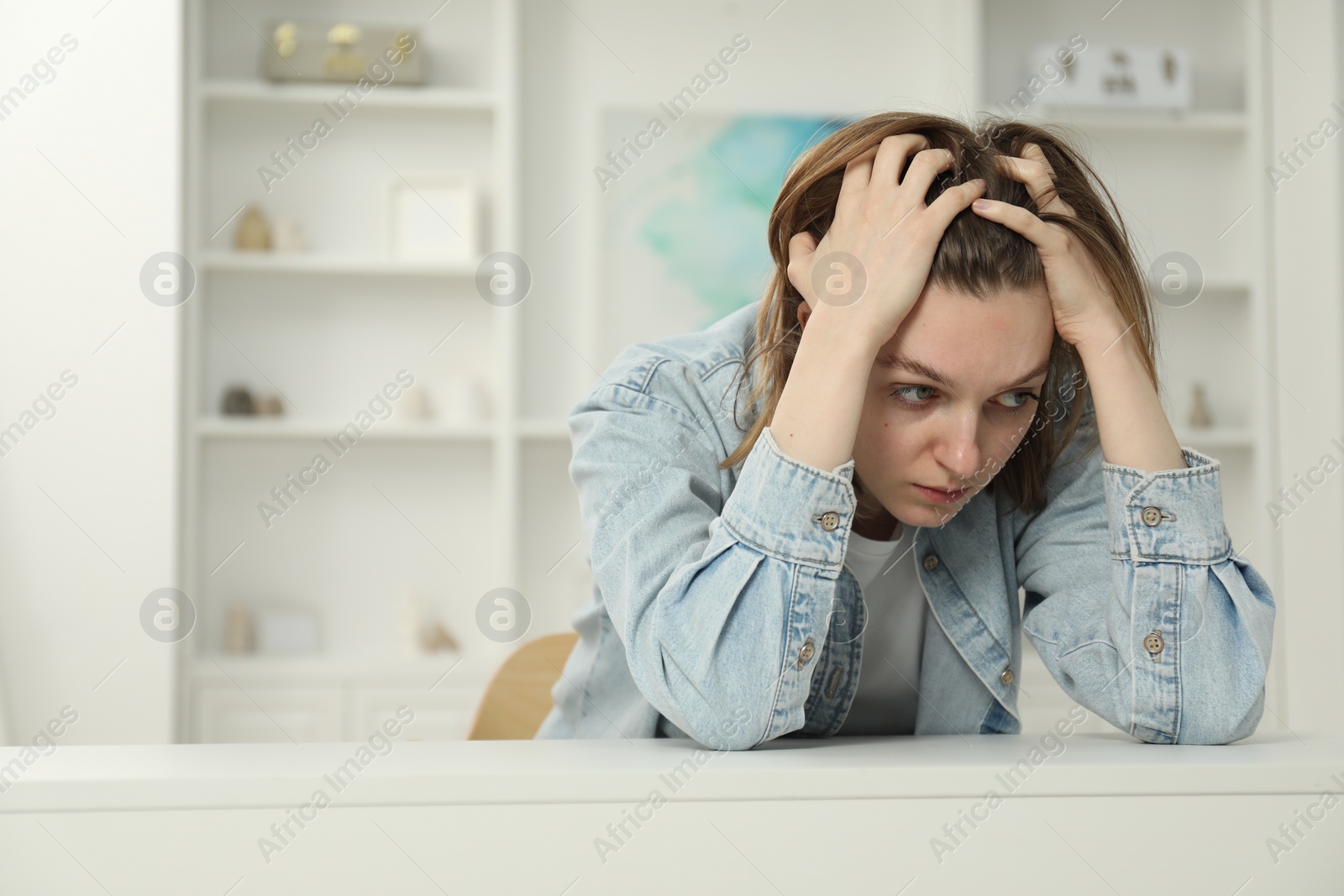 Photo of Sad young woman sitting at white table in room, space for text