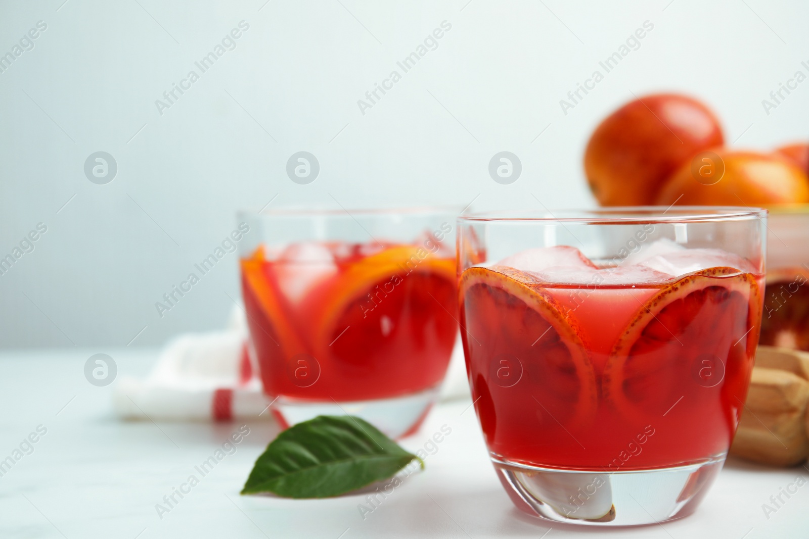 Photo of Tasty sicilian orange juice with ice cubes and fruits on white table, space for text