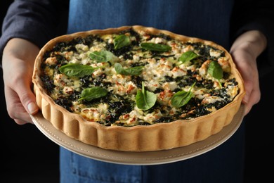 Photo of Woman holding delicious homemade spinach quiche on dark background, closeup