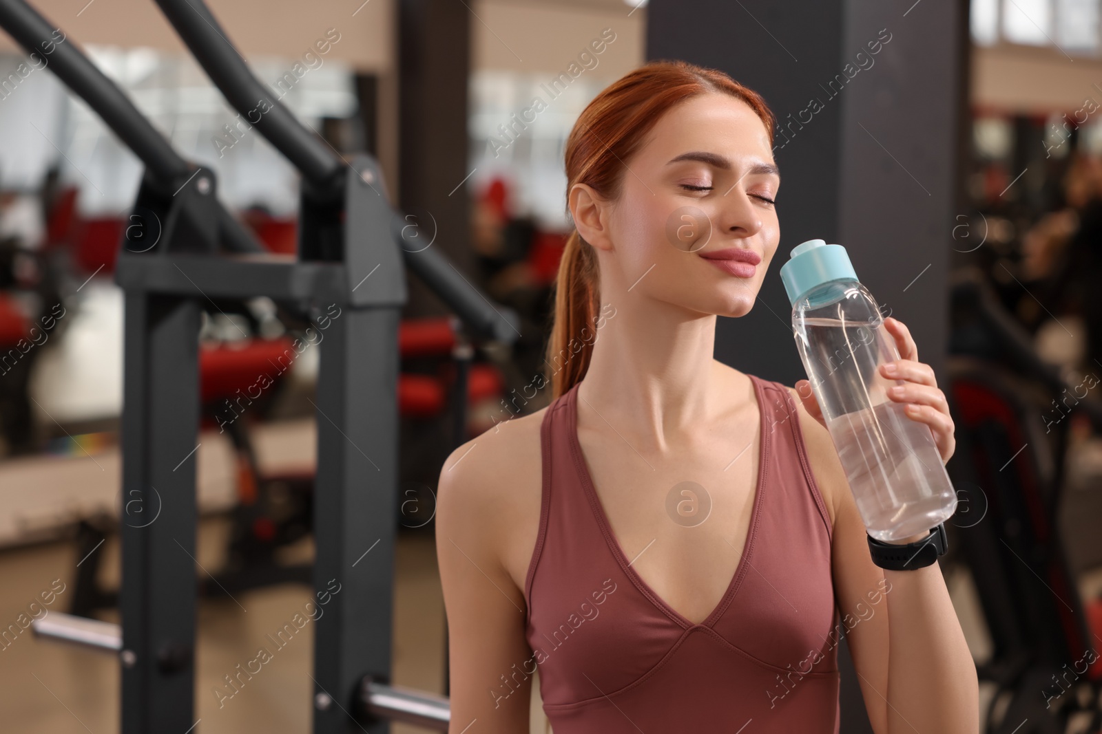 Photo of Beautiful young woman with bottle of water in gym, space for text