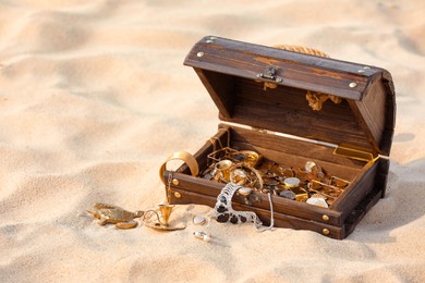 Photo of Open wooden treasure chest on sand, space for text