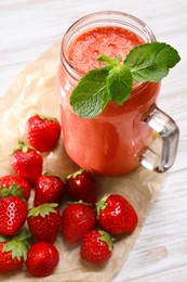 Photo of Mason jar of tasty smoothie and fresh strawberries on white wooden table, above view