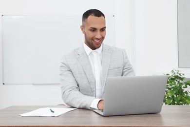 Photo of Happy young intern working with laptop at table in modern office