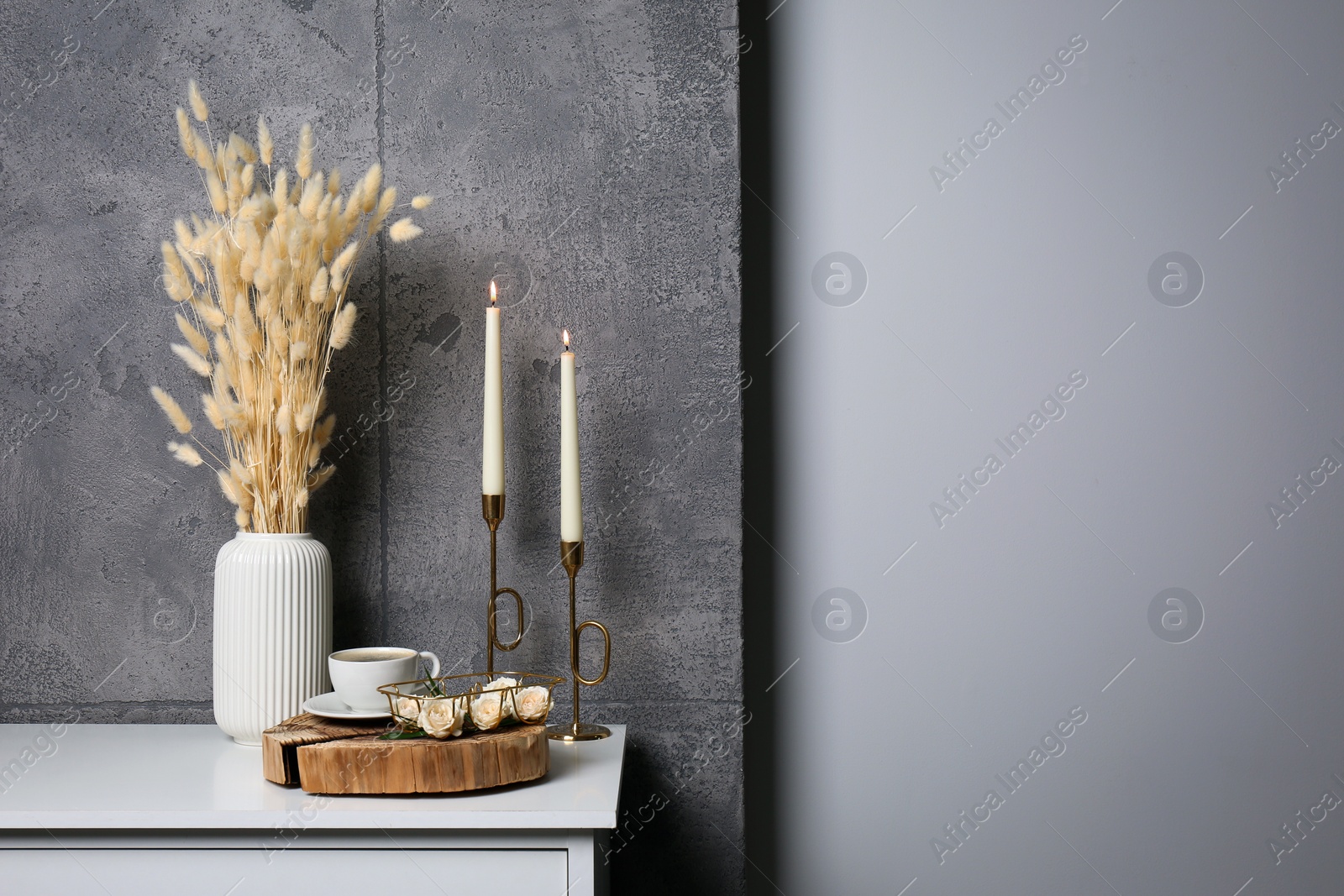 Photo of Cup of coffee, vase and other decor on white table near grey wall indoors, space for text. Interior design