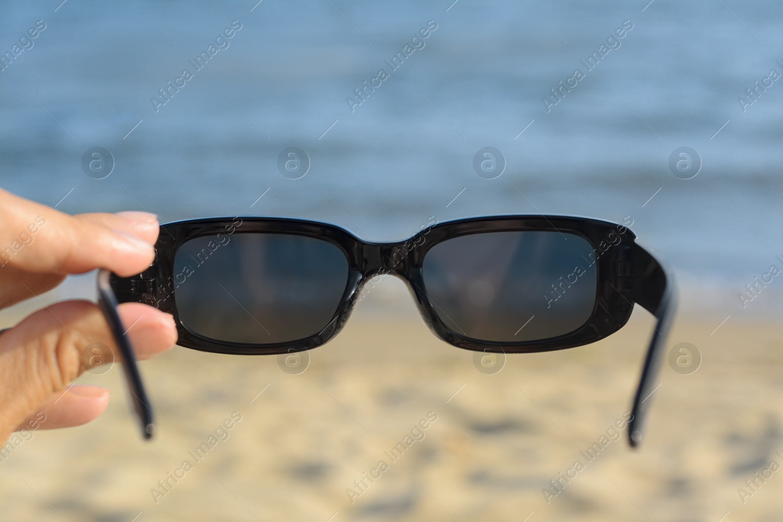 Photo of Woman holding stylish sunglasses near beautiful sea, closeup