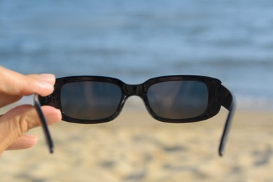 Photo of Woman holding stylish sunglasses near beautiful sea, closeup