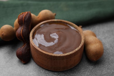 Photo of Bowl of tamarind sauce and fresh pods on brown table, closeup