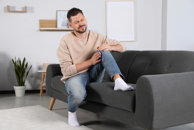 Photo of Man suffering from knee pain on sofa at home