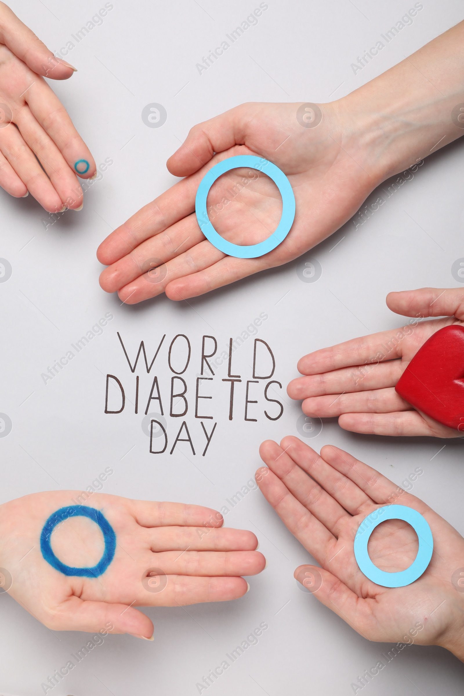 Photo of People showing blue circles and red heart near text World Diabetes Day on light background, top view