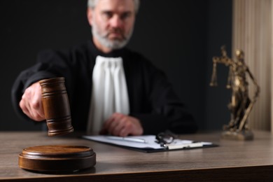 Photo of Judge with gavel and papers sitting at wooden table against black background, selective focus