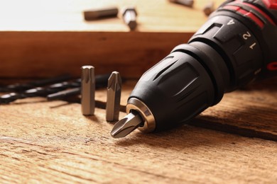 Photo of Electric screwdriver with bits and drills on wooden table, closeup
