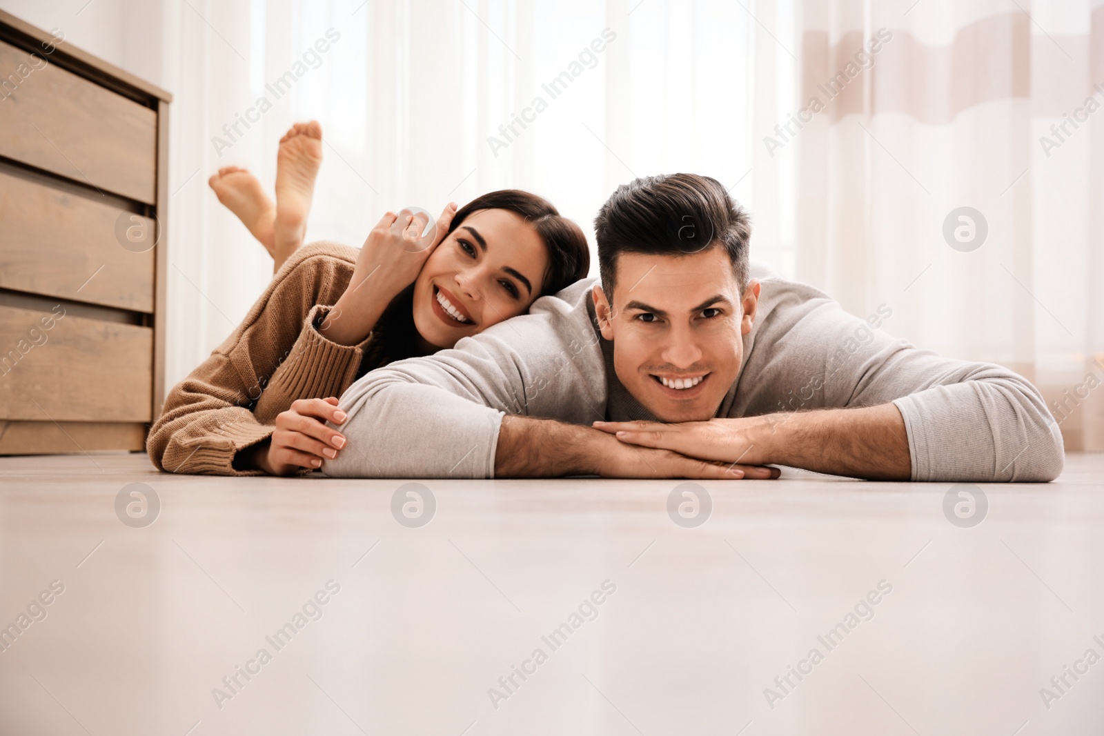 Photo of Happy couple lying on warm floor at home. Heating system