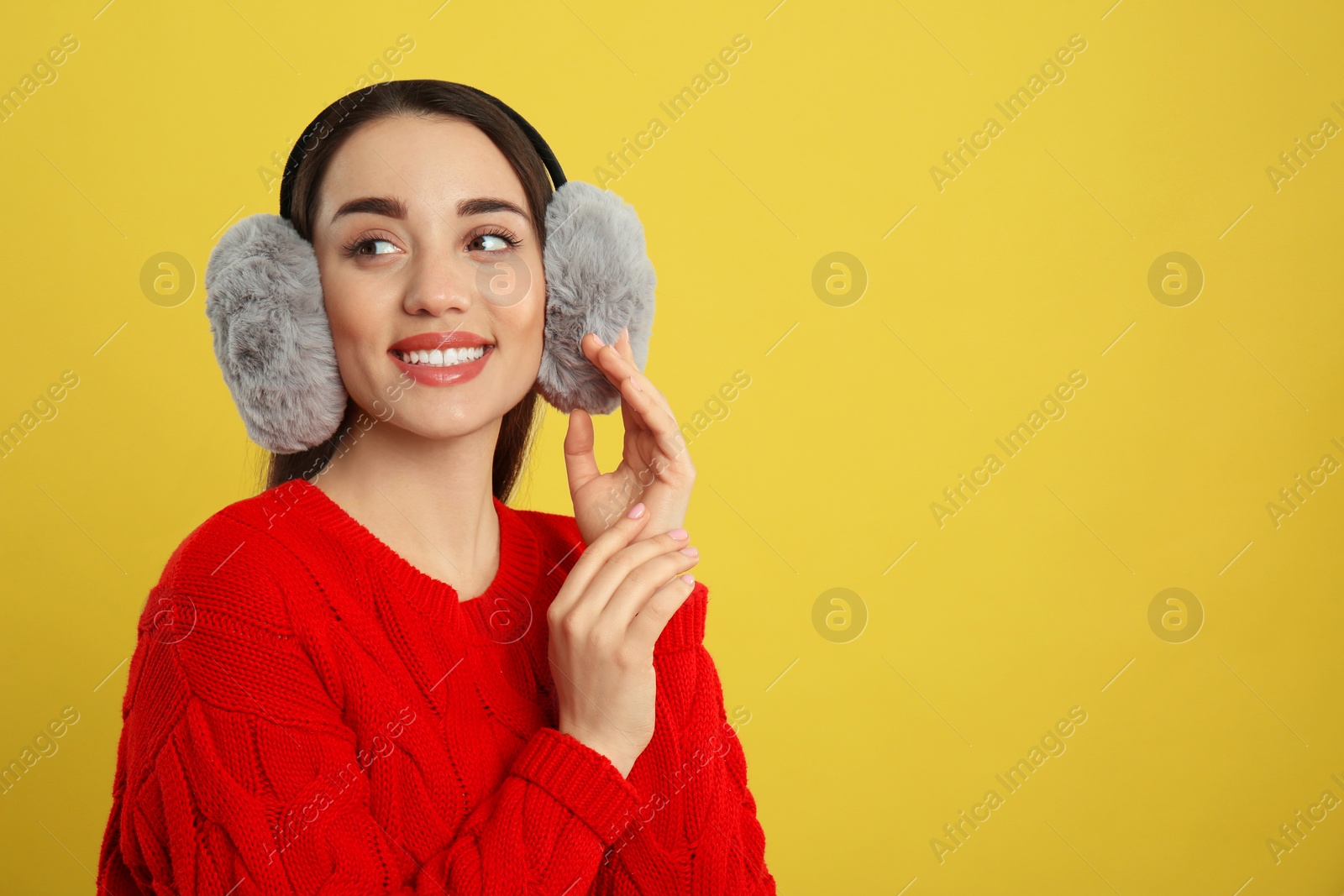 Photo of Beautiful young woman wearing earmuffs on yellow background. Space for text