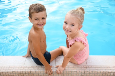 Photo of Cute little children sitting at outdoor swimming pool