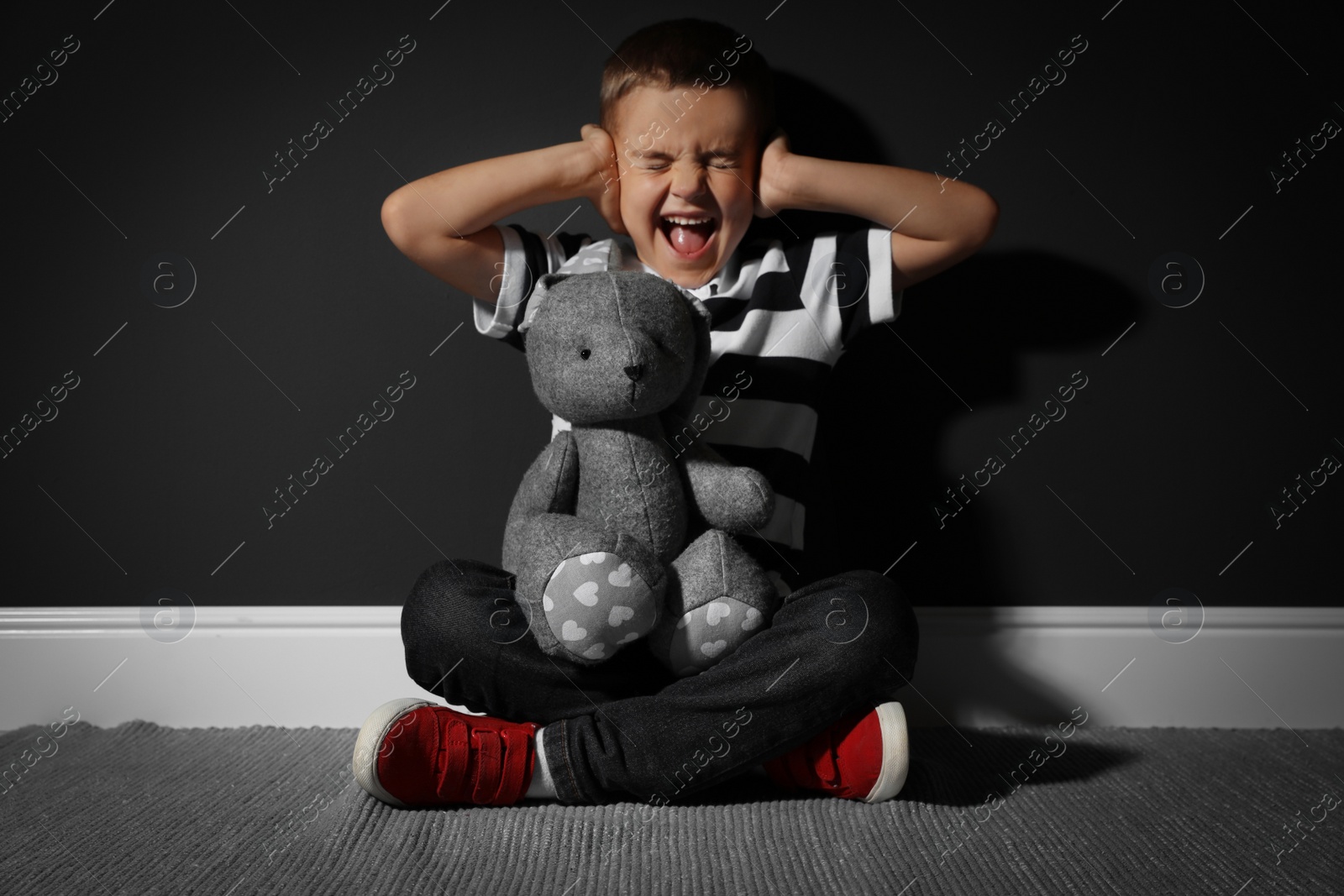 Photo of Scared little boy with toy near black wall. Domestic violence concept
