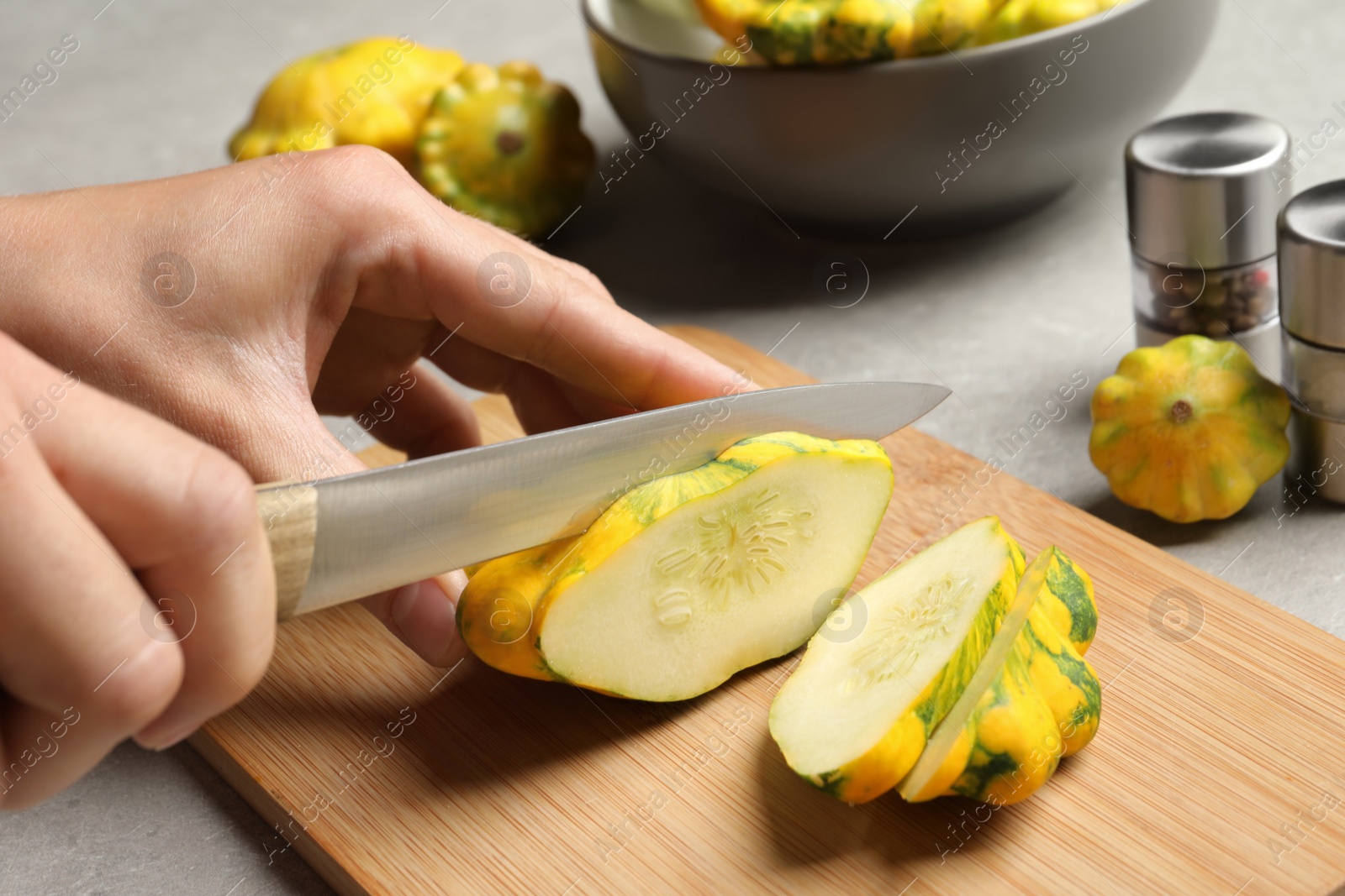 Photo of Woman cutting ripe yellow pattypan squash at grey table, closeup