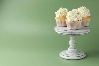 Tasty vanilla cupcakes with cream on green background, space for text