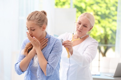 Doctor examining coughing young woman at clinic