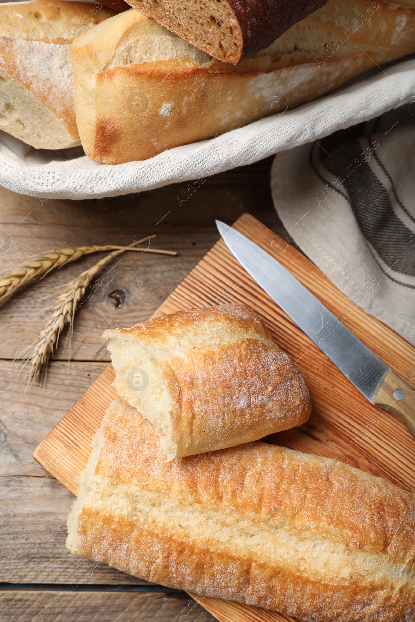 Photo of Different tasty baguettes, knife and spikelets on wooden table, flat lay