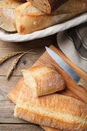 Photo of Different tasty baguettes, knife and spikelets on wooden table, flat lay