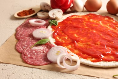 Photo of Pizza base smeared with tomato sauce and products on light textured table, closeup