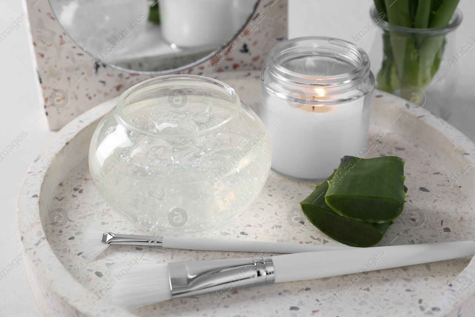 Photo of Jar of natural gel, burning candle, makeup brushes and sliced aloe leaves on table, closeup