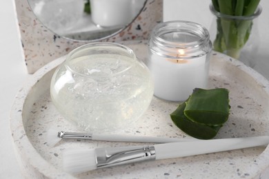 Photo of Jar of natural gel, burning candle, makeup brushes and sliced aloe leaves on table, closeup