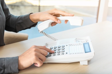 Photo of Woman dialing number on telephone at table in office