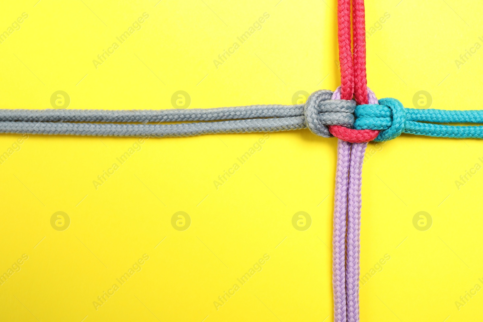 Photo of Top view of colorful ropes tied together on yellow background, space for text. Unity concept