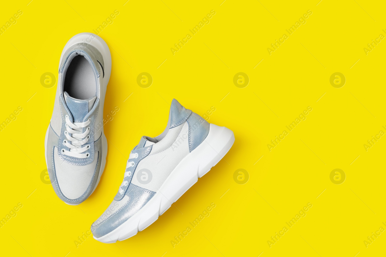 Photo of Stylish sneakers on yellow background, flat lay. Space for text