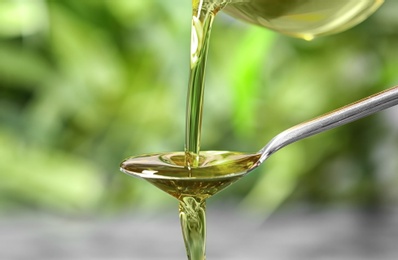 Pouring hemp oil into spoon on blurred background, closeup