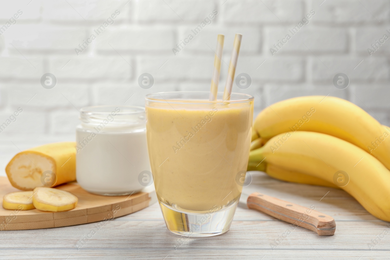 Photo of Glass of tasty banana smoothie with straws and ingredients on white wooden table