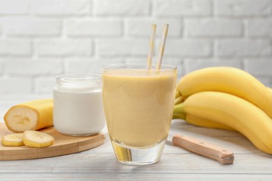 Photo of Glass of tasty banana smoothie with straws and ingredients on white wooden table