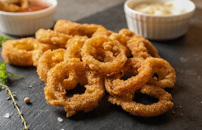 Photo of Homemade crunchy fried onion rings and sauces and sauces on slate plate, closeup