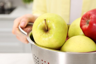 Photo of Woman holding colander with fresh apples at table indoors, closeup