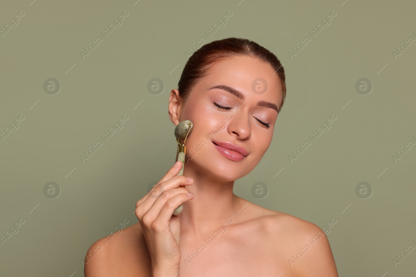 Photo of Young woman massaging her face with jade roller on green background