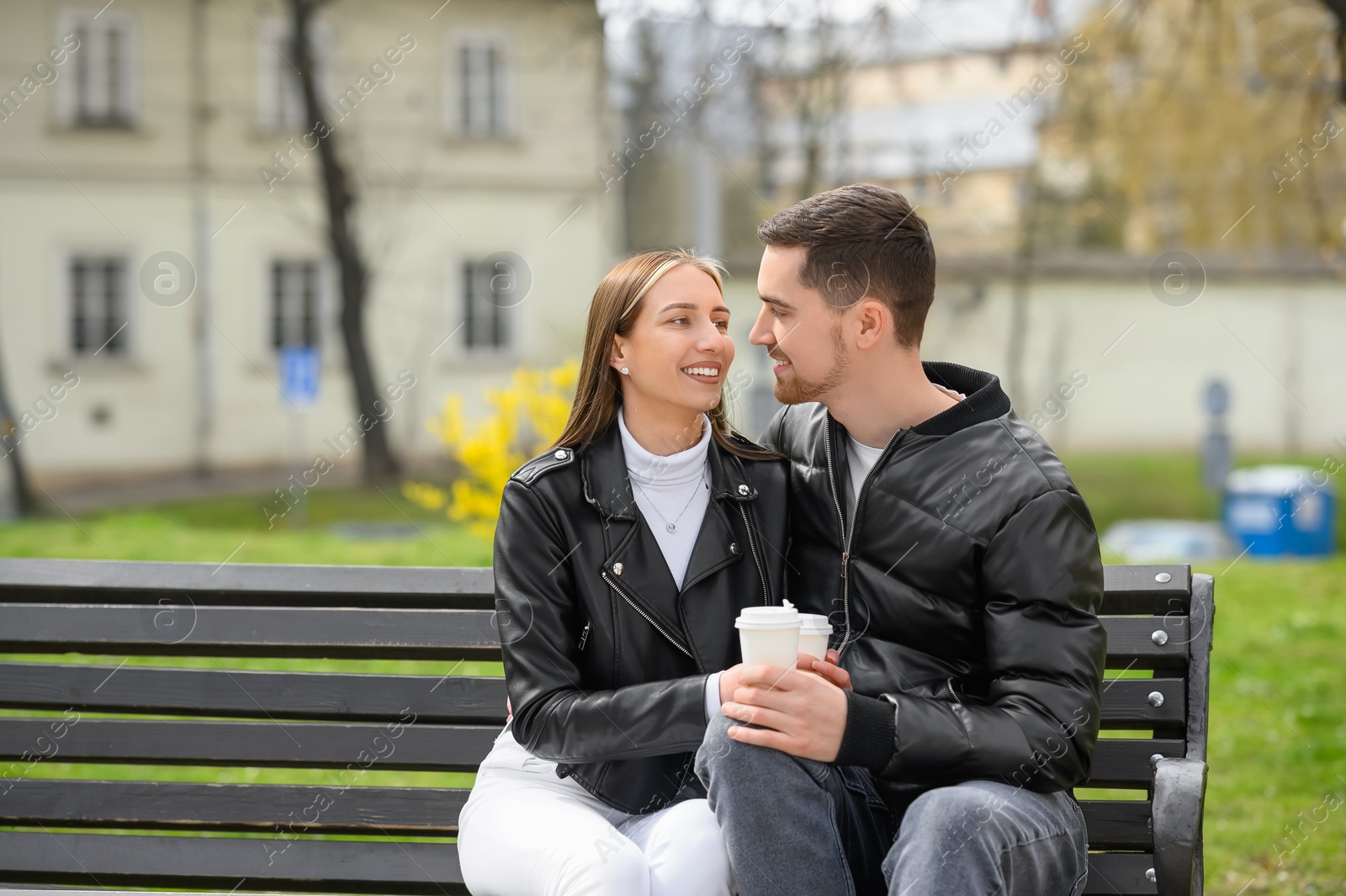 Photo of Lovely young couple with cups of coffee on bench outdoors. Romantic date